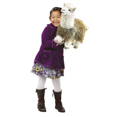 Smiling girl wearing a purple jacket holds a fluffy alpaca hand puppet against a white background.