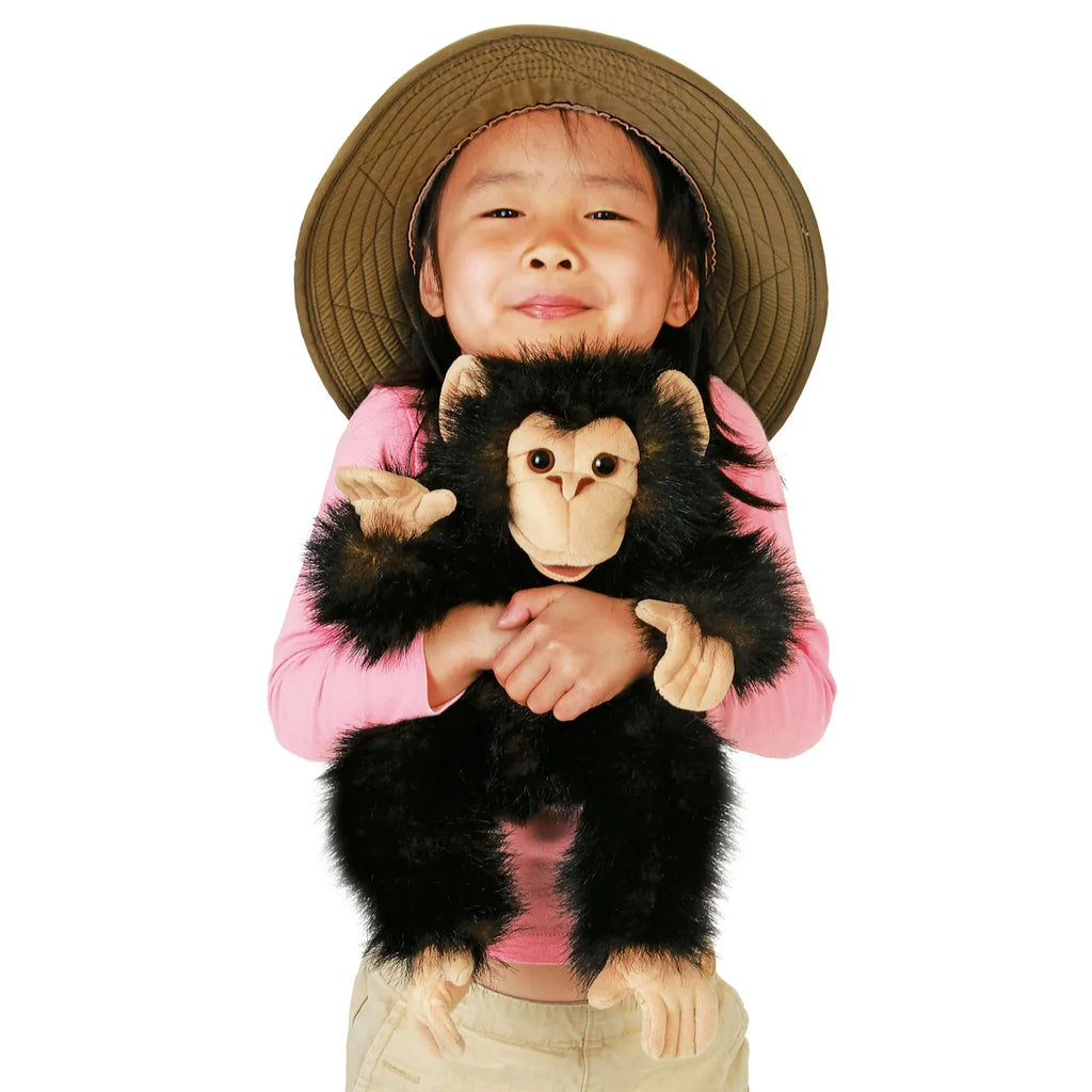 A smiling child in a wide-brimmed hat and pink shirt hugs a plush chimp toy. The child displays joy and warmth, conveying a playful and affectionate mood.