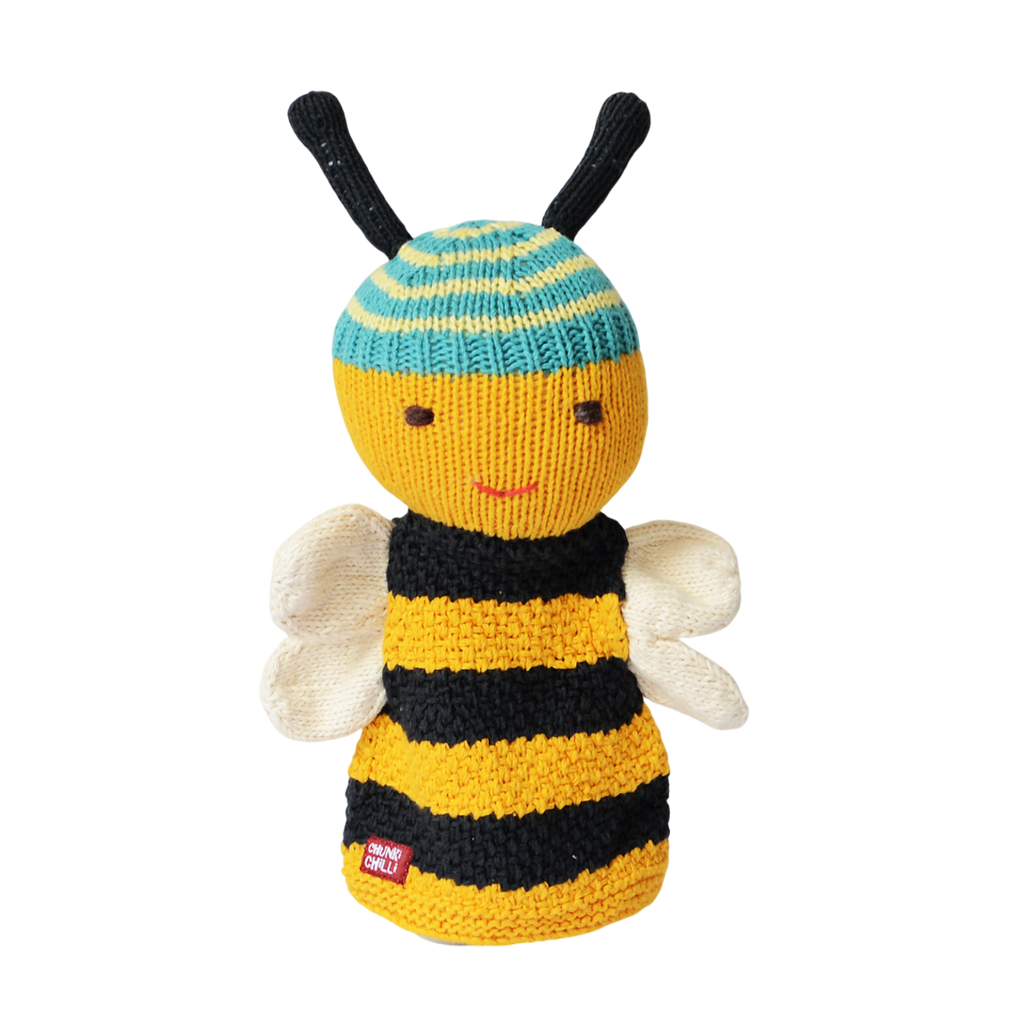Smiling knitted bee toy with a striped yellow and black body, blue and yellow head with antennae, and white wings, on a white background. Cheerful tone.