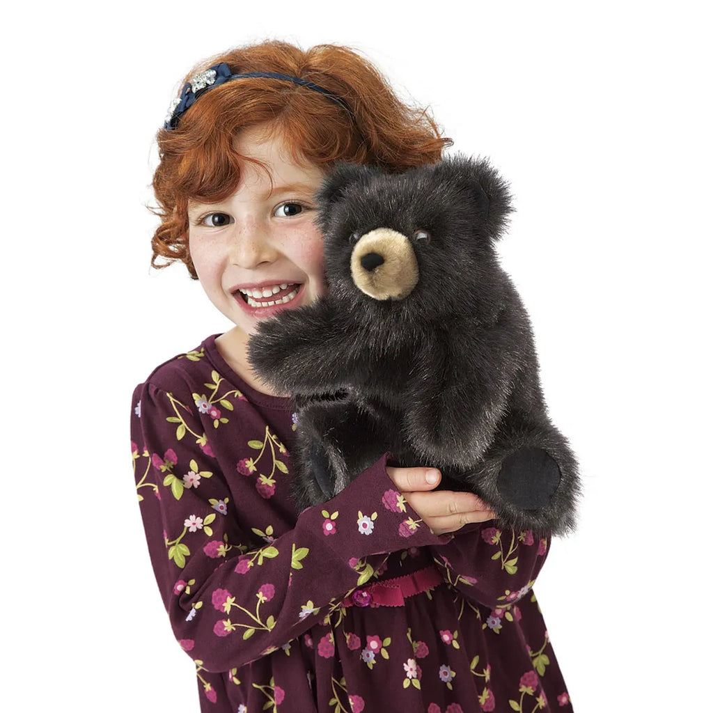 A smiling child with curly red hair holds a plush bear. She wears a floral dress, adding a cheerful and playful tone to the scene.