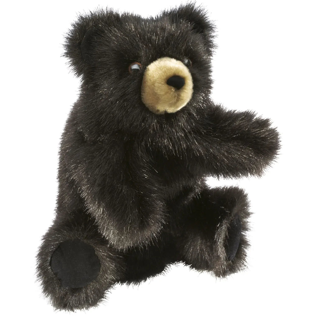 A fuzzy black teddy bear with a beige snout sits upright, its right paw raised playfully. The bear's inviting appearance exudes warmth and comfort.