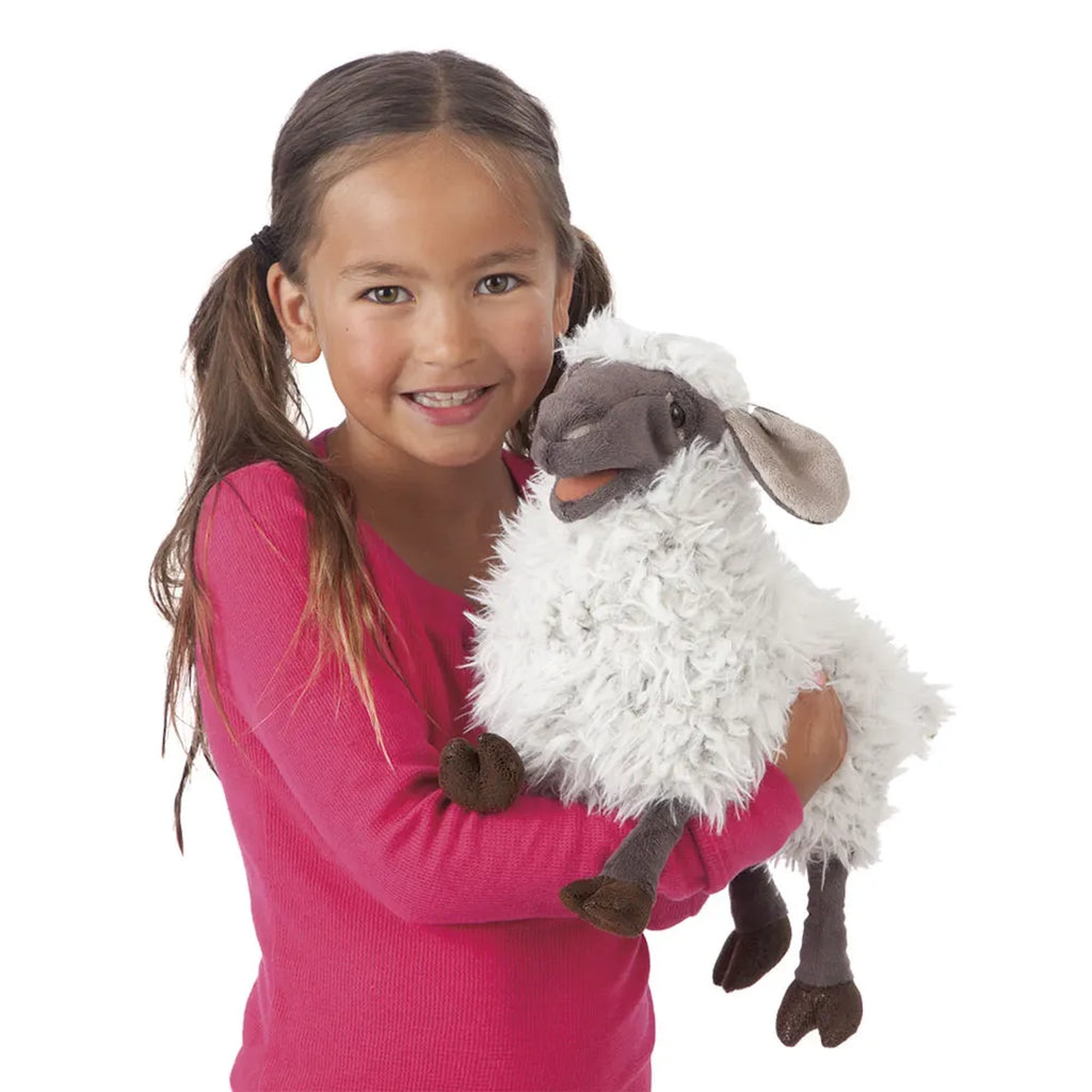 A smiling young girl in a pink shirt holding a fluffy sheep plush toy. The toy has a gray face and ears, conveying a cheerful and playful mood.