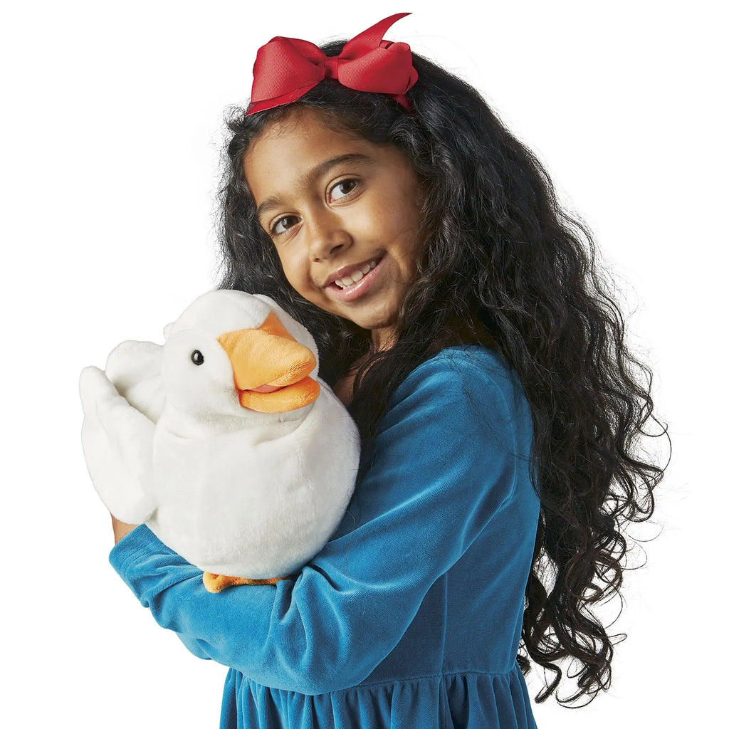 A young girl with a red bow holds a plush white duck, smiling warmly. She wears a blue dress, set against a plain white background, conveying joy.