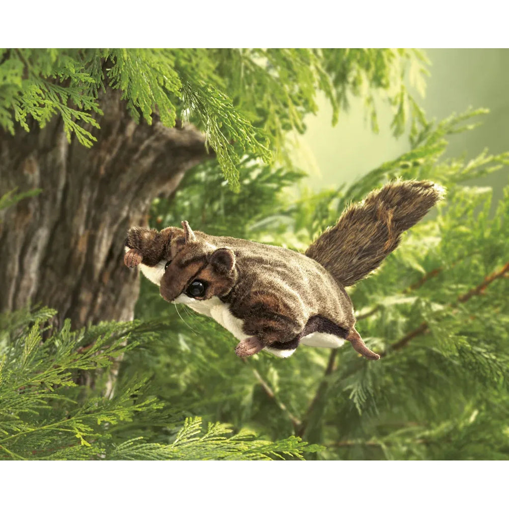 A flying squirrel glides among lush green foliage and a tree trunk. Its limbs are spread wide, fur lightly ruffled, evoking a sense of freedom.