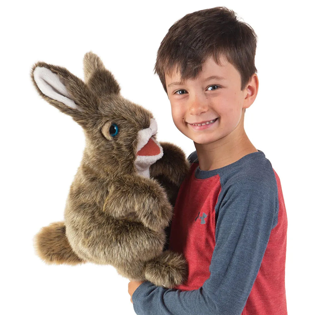 A young boy in a red and blue shirt smiles while holding a large, fluffy rabbit puppet. The scene is cheerful and playful, highlighting friendship.
