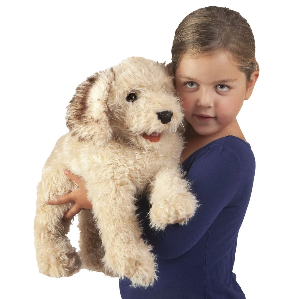 A child in a blue shirt lovingly holds a large, fluffy stuffed dog with beige fur and brown ears, conveying warmth and affection against a white background.