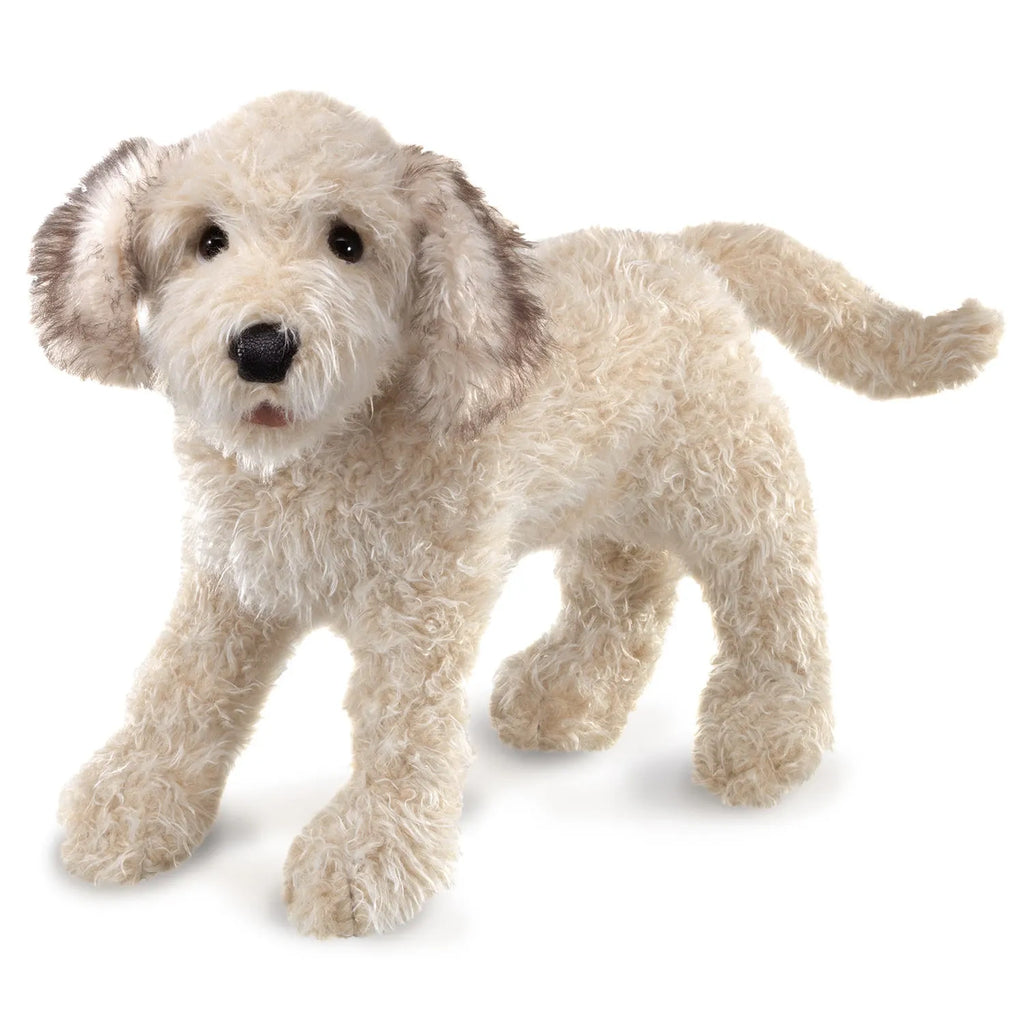 Fluffy plush toy dog with cream-colored fur and dark ears stands on all fours, conveying a playful and lifelike appearance against a white background.