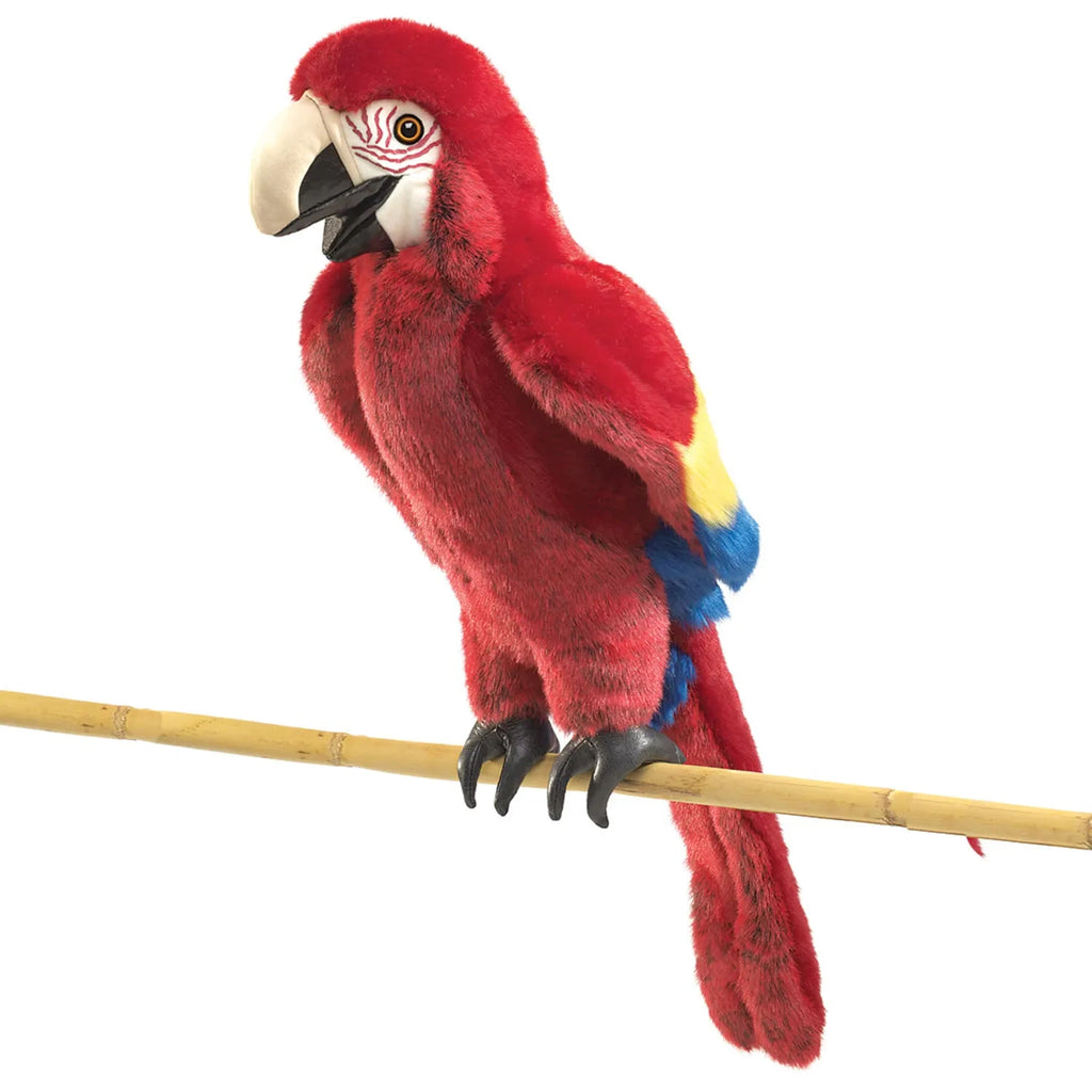 A vibrant scarlet macaw puppet with red, yellow, and blue feathers perches on a wooden stick, conveying a playful and lively tone.