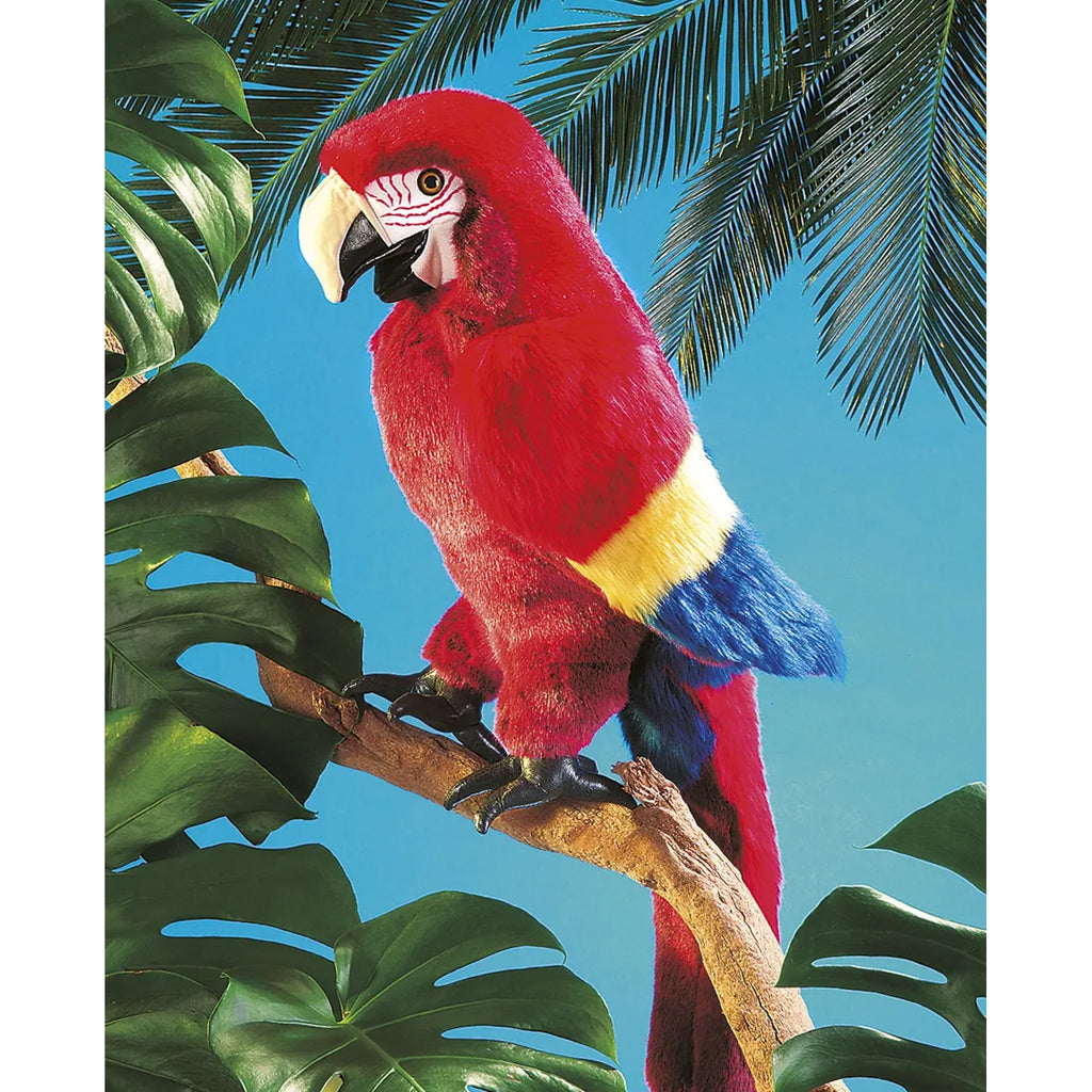 A vibrant parrot with red, yellow, and blue feathers perches on a branch. It is surrounded by lush, green tropical leaves against a bright blue sky.