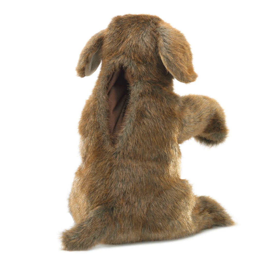 A furry brown puppet resembling a dog, seen from the back. It has floppy ears, a hole for manipulating, and soft fur, evoking a playful tone.