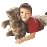 Smiling boy lying down and hugging a brown dog hand puppet.