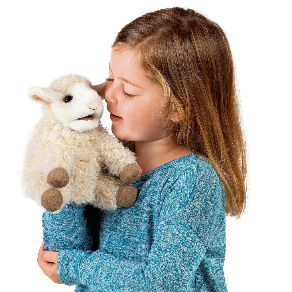 A young girl in a blue sweater holds a plush lamb puppet closely. She gazes affectionately at it, conveying warmth and innocence.