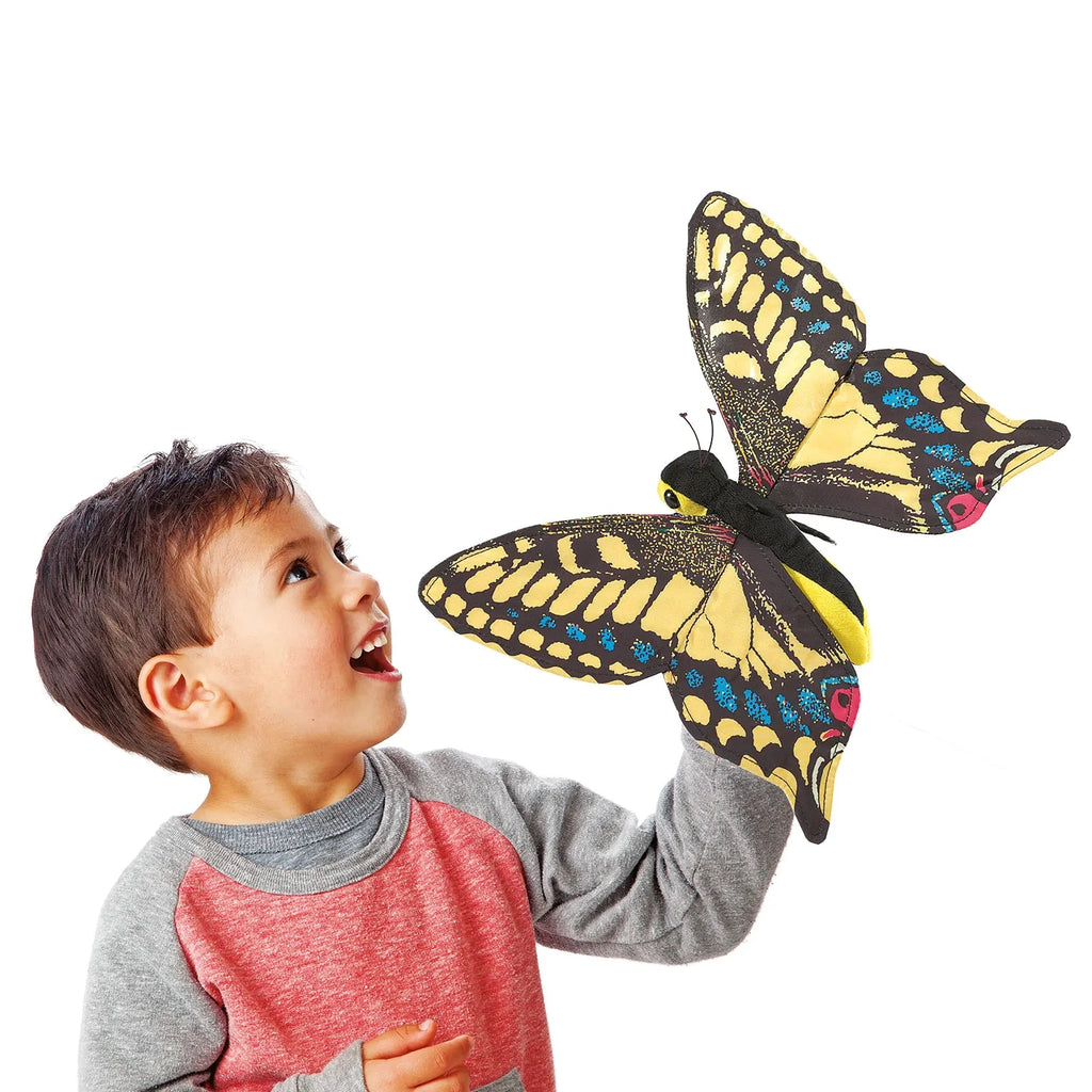 A smiling child in a red and gray sweater holds an oversized, colorful butterfly puppet. The child's expression conveys wonder and excitement.