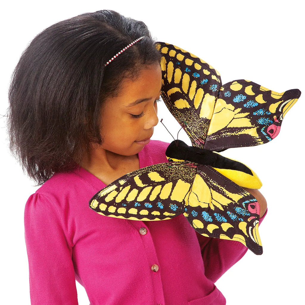 A young girl in a pink sweater gently holds a large, colorful butterfly puppet. The butterfly has vibrant yellow and black wings with blue accents.