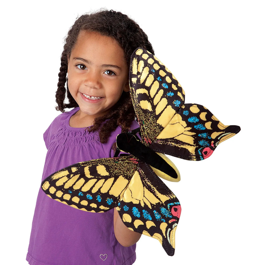 A cheerful child in a purple shirt holds a large, colorful butterfly puppet with vibrant yellow, blue, and red markings, portraying joy and playfulness.