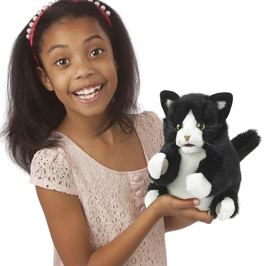 Smiling girl holds a black and white stuffed cat toy. She wears a pink lace dress and a red headband with pearls, conveying joy and playfulness.