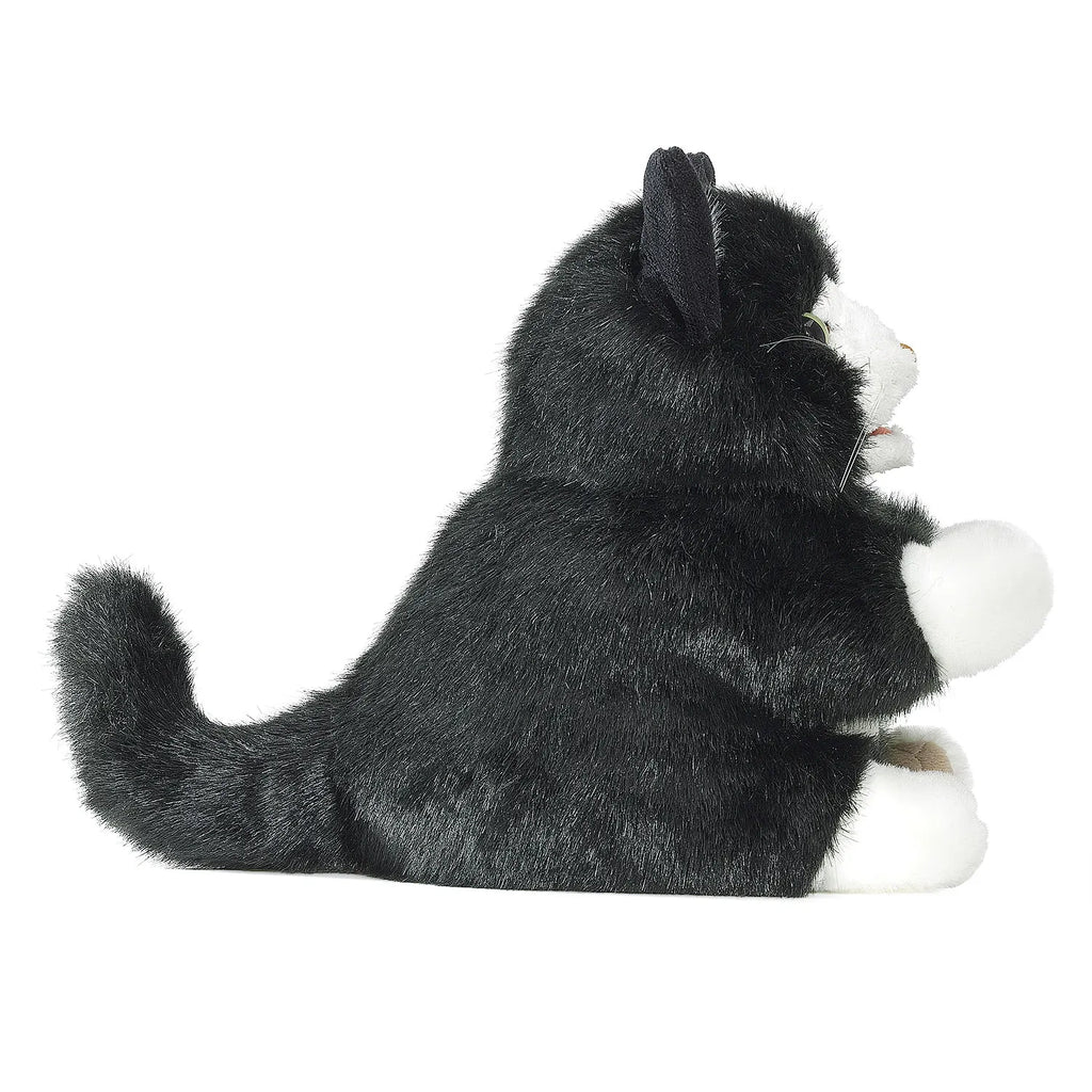 Black and white plush cat toy sitting upright, viewed from the side. The toy features a fluffy tail, black ears, and white paws, conveying a playful appearance.
