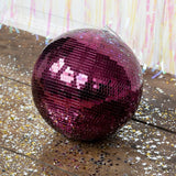 A shiny plum purple disco ball sits on a wooden floor covered in silver star confetti.