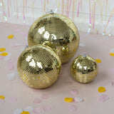 Three shimmering gold disco balls of different sizes are arranged on a light pink surface scattered with yellow, white, and pink confetti.