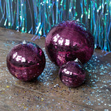 Three plum purple disco balls of varying sizes on a wooden floor covered in silver star glitter.