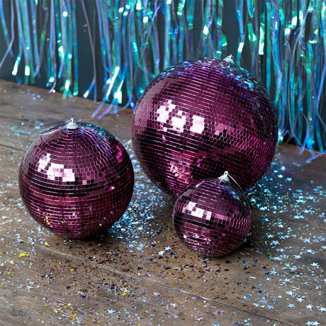 Three plum purple disco balls of varying sizes on a wooden floor covered in silver star glitter.
