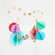 Gold "Happy Birthday" cake topper with colorful honeycomb balls, paper fans, and shooting star wire toppers.