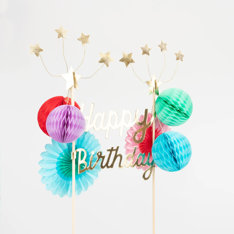Gold "Happy Birthday" cake topper with colorful honeycomb balls, paper fans, and shooting star wire toppers.