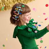 A young girl wearing colorful hair clips while surrounded by falling confetti.