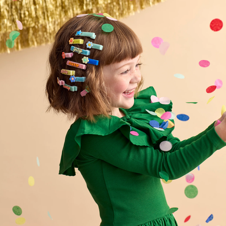 A young girl wearing colorful hair clips while surrounded by falling confetti.