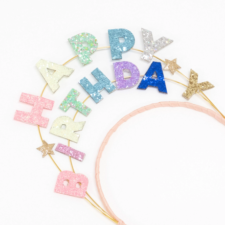 Close-up view of the Meri Meri glitter headband spelling "Happy Birthday" with colorful letters and small star accents.
