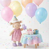 Dinkum Doll in pink dress and party hat celebrating a birthday with balloons, plush cake, and gifts.