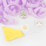 Unwrapped surprise ball gifts showing a rainbow charm, stickers, party hat, joke slip, and purple streamer.