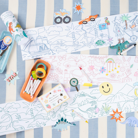 Meri Meri coloring rolls spread out with crayons, stickers, and cutouts on a striped surface.
