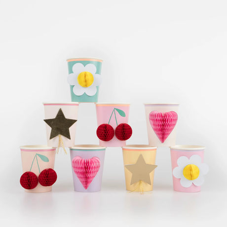 An assortment of Meri Meri party cups stacked in a pyramid shape, featuring various colorful 3D honeycomb and gold foil designs.
