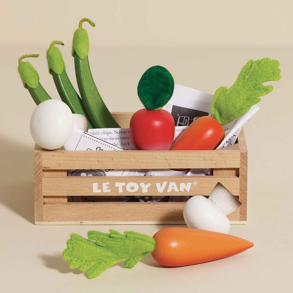 A wooden crate labeled "Le Toy Van" holds toy vegetables on a white background. Playful tone.