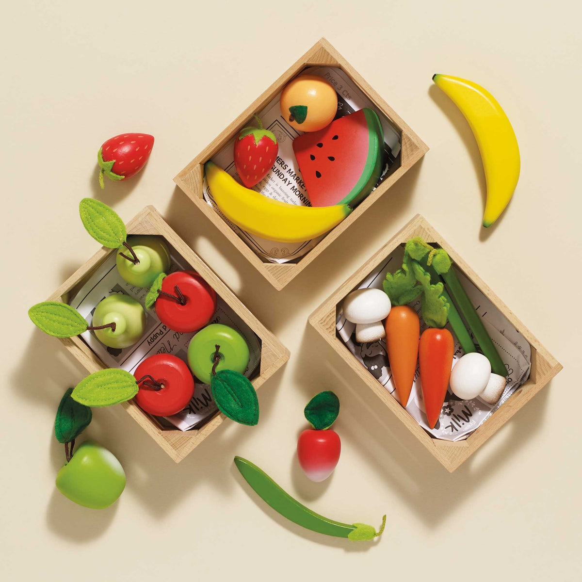 Three wooden crates filled with play fruits, apples, and vegetables on a beige surface.