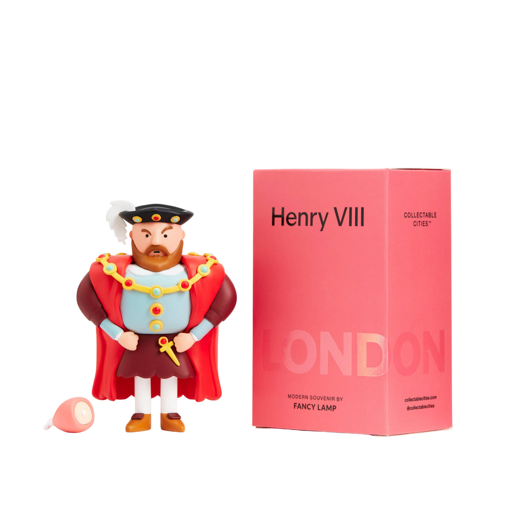 Toy figure of a regal man with a beard, red cape, and black hat stands beside a pink box labeled "Henry VIII." A small ham lies on the ground.