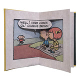Peanuts pop-up book page showing Charlie Brown walking toward characters with a speech bubble saying his name.