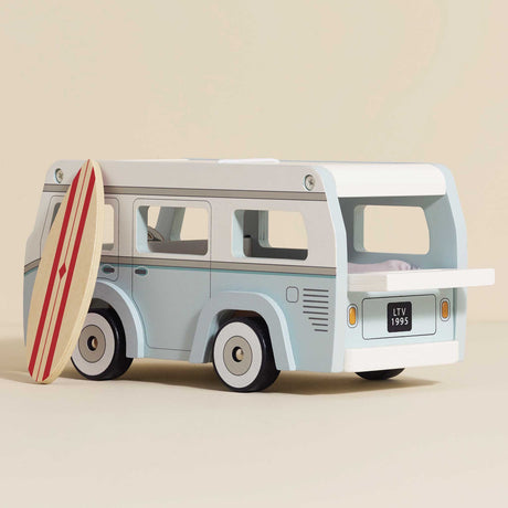 Light blue and white wooden toy camper van leaning against a toy surfboard with red stripes.
