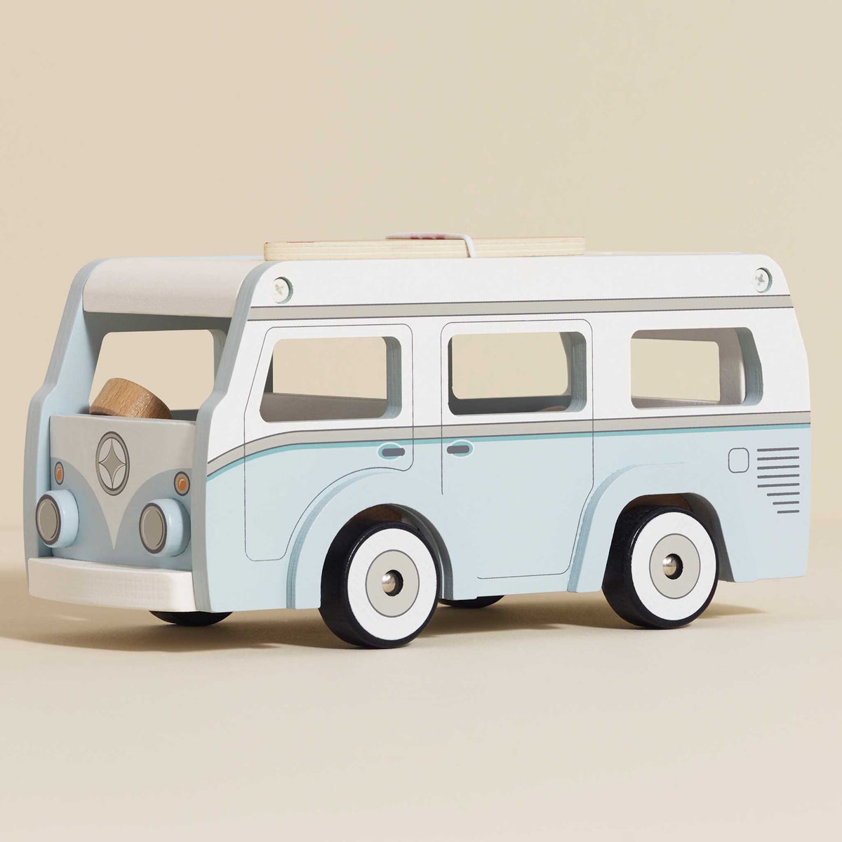 Light blue and white wooden toy camper van with surfboard on roof, side view.