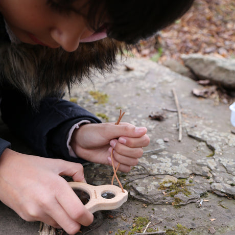 Child using a Huckleberry wooden dual magnifier to explore moss and rocks outdoors, nature study and educational toy.