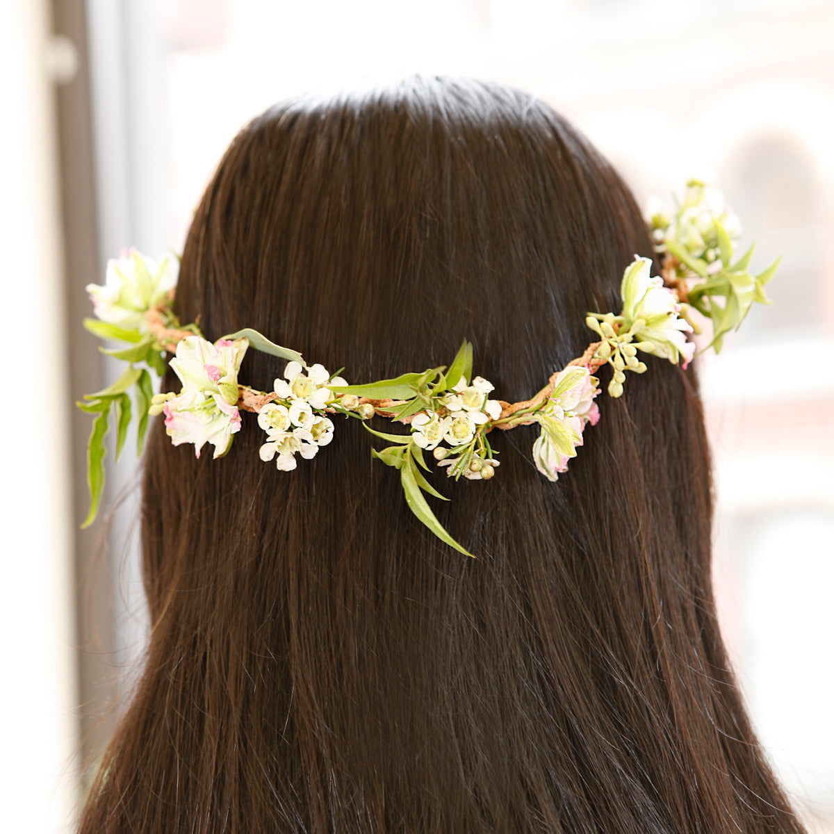 Back view of a person with long dark hair wearing a delicate DIY flower crown made of small white and pink blossoms.