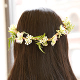 Back view of a person with long dark hair wearing a delicate DIY flower crown made of small white and pink blossoms.