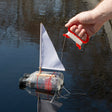 A homemade toy sailboat made from recycled plastic bottles floating on water with a control line held by a person.
