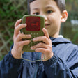 Child using a Huckleberry Morse Code Light toy outdoors to send signals using the printed alphabet guide.