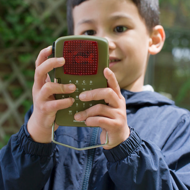 Child using a Huckleberry Morse Code Light toy outdoors to send signals using the printed alphabet guide.