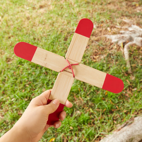 Hand holding a Huckleberry bamboo pocket boomerang with red tips in a grassy outdoor park setting.