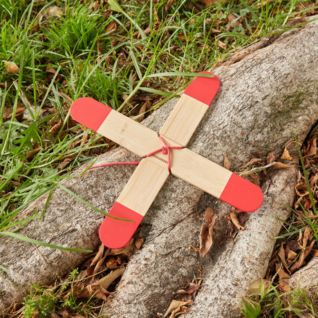 Huckleberry bamboo pocket boomerang with red tips resting on a wooden log in a grassy outdoor setting.