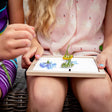 Kids arranging blue and yellow wildflowers in Huckleberry pressed flower wood frame craft kit outdoors.