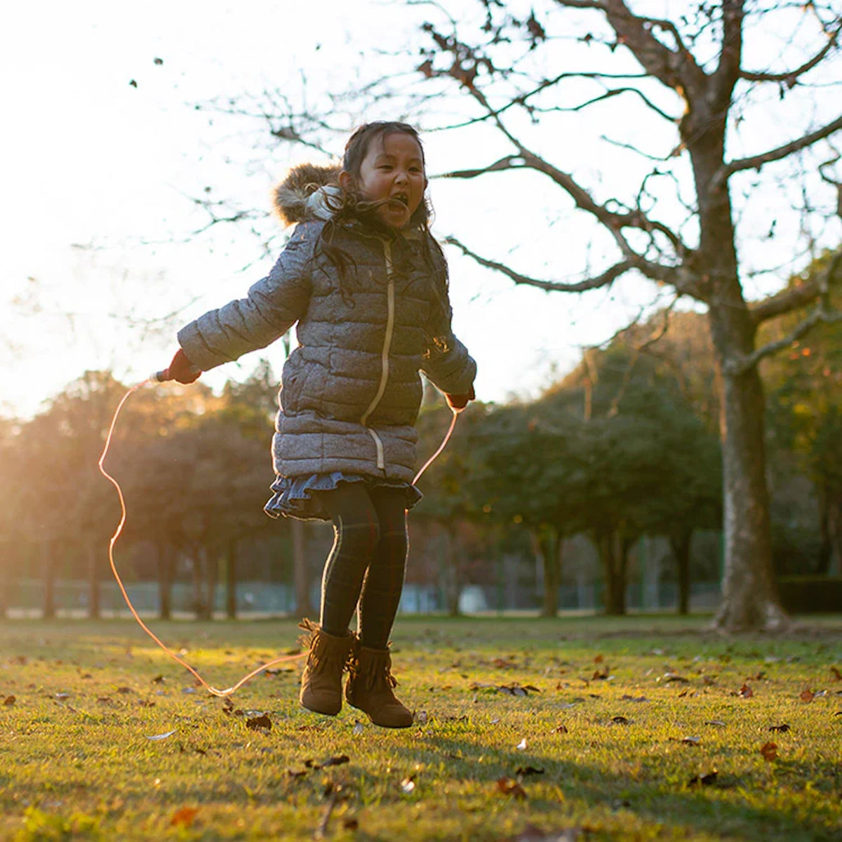 Happy young girl jumping rope in a park during autumn with trees and golden hour sunlight.